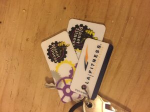 Three plastic tags on a keychain (two for planet fitness, one for LA Fitness) with a key and a hair elastic.