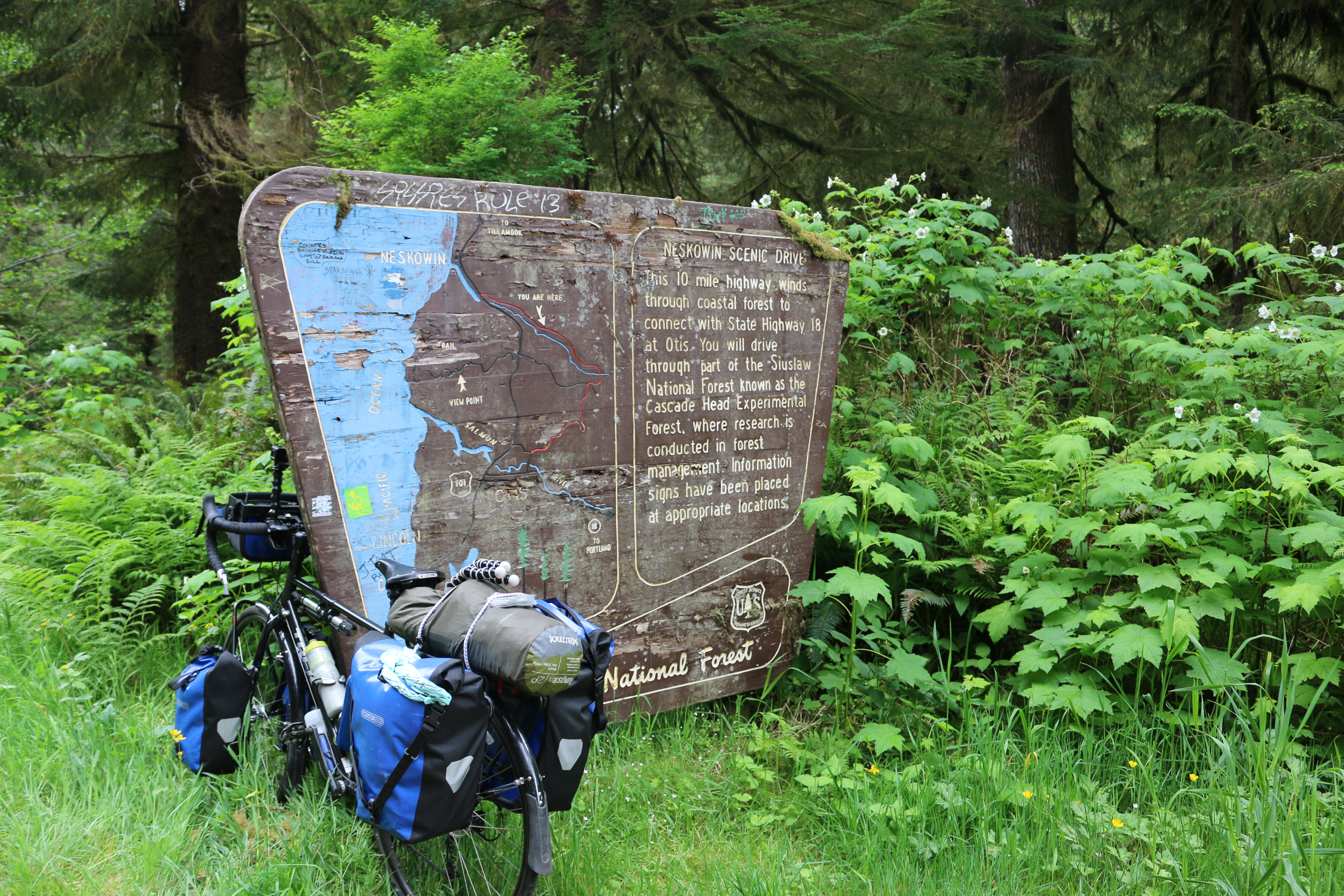 Loaded bike learning up against an old sign showing a map and description of the Neskowin Scenic Drive