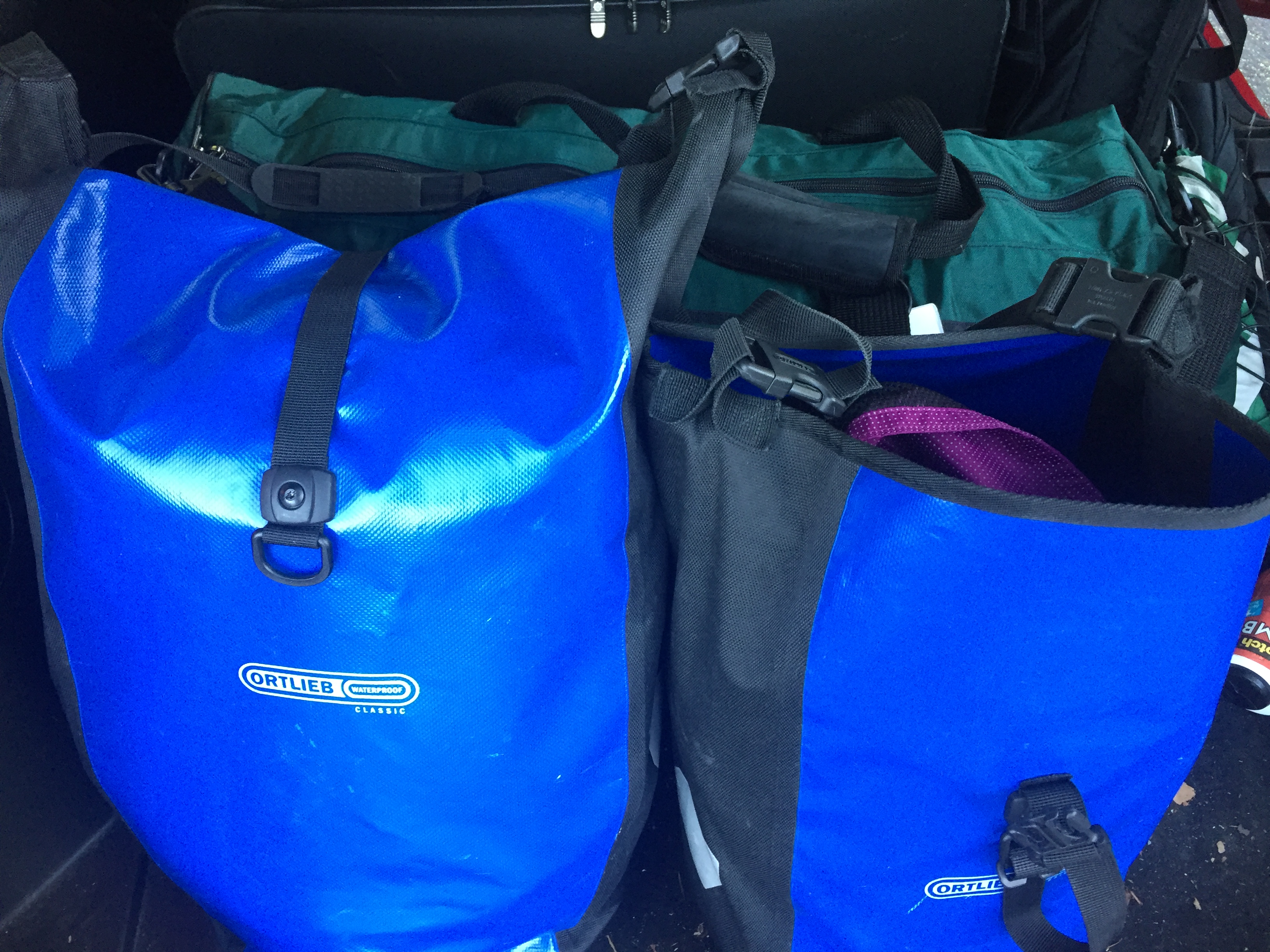 A long, green duffel bag with two blue ortlieb panniers in the foreground.